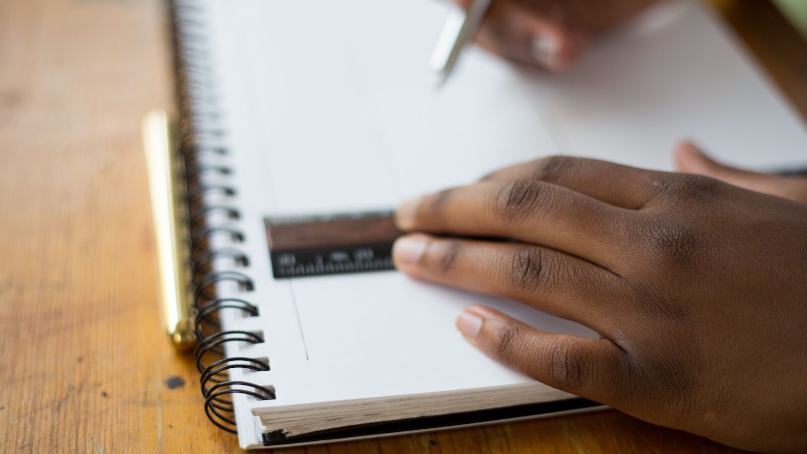 person holding ruler and pencil on spiral notebook